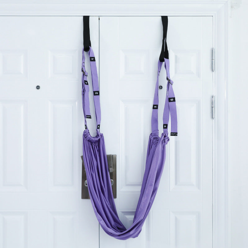 A person using a purple yoga inversion and stretching strap to assist with a yoga pose, hanging from a door frame.