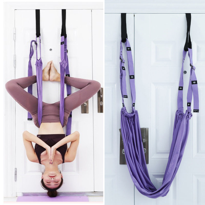 Person practicing yoga using a purple aerial yoga hammock against a white door.