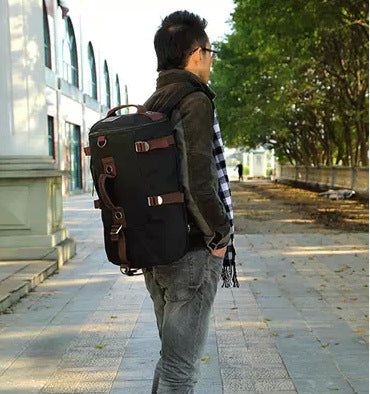 Person wearing a black backpack on a sidewalk with trees and buildings in the background